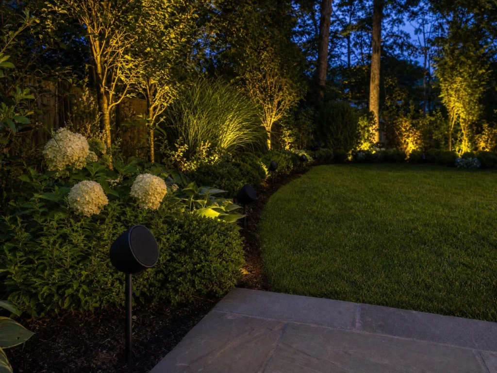 Back yard at dusk with small staked speakers spaced along the planting beds.